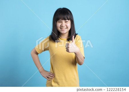 An Asian girl gives a thumbs up and smile on blue background. An Asian girl gives a thumbs up and smile on blue background. 122228154