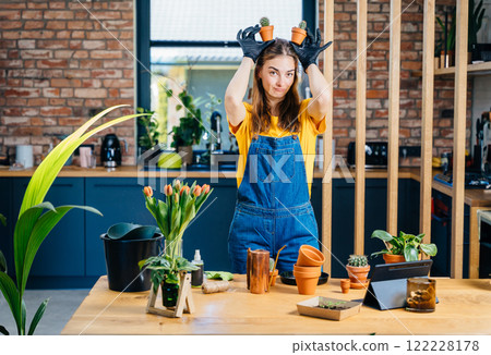 Having Fun Growing Plants Concept. Playful young female holds small succulents plants in pots like ears at cozy home with modern kitchen interior on background. Having Fun Growing Plants Concept. Playful young female holds small succulents plants in pots like ears at cozy home with modern kitchen interior on background. 122228178
