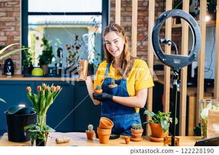 Emotional portrait of European woman plant lover holding two small freshly transplanted cactuses in potted. Daily chores, cute woman, mini cactus garden, warm home kitchen backdrop. 122228190