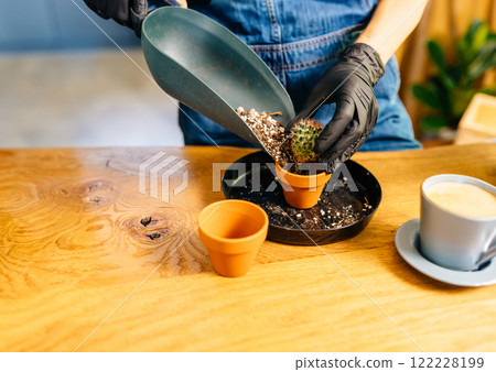 Close up of hands in gloves of unrecognizable housewife fills ceramic pot with soil to plant seedlings representing home gardening as a hobby. Concept of home garden. Spring time. Close up of hands in gloves of unrecognizable housewife fills ceramic pot with soil to plant seedlings representing home gardening as a hobby. Concept of home garden. Spring time. 122228199