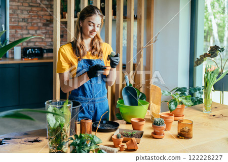 Pretty female wearing overalls gardening at home. Home planting on the kitchen. Free time for little house gardening concept. Pretty female wearing overalls gardening at home. Home planting on the kitchen. Free time for little house gardening concept. 122228227