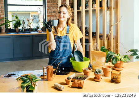 Happy woman enjoy coffee break at home modern interior taking care of plants with gardening material. Concept of home garden. Spring time. Stylish interior with plants. Taking care of plants. Template Happy woman enjoy coffee break at home modern interior taking care of plants with gardening material. Concept of home garden. Spring time. Stylish interior with plants. Taking care of plants. Template 122228249