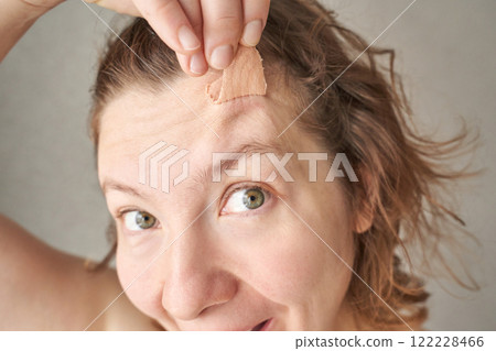 Young caucasian female applying adhesive bandage to forehead wound with smiling Young caucasian female applying adhesive bandage to forehead wound with smiling 122228466