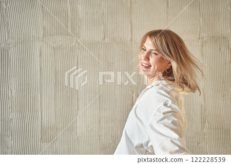 Caucasian female adult smiling with wind in hair against textured wall 122228539
