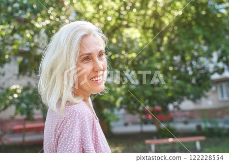 Caucasian mature female smiling outdoors with trees in background on a sunny day 122228554