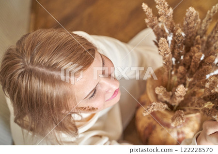 Young caucasian female admiring rustic floral arrangement in warm indoor setting Young caucasian female admiring rustic floral arrangement in warm indoor setting 122228570