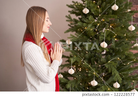 Young caucasian woman in cozy white sweater enjoying christmas tree with lights Young caucasian woman in cozy white sweater enjoying christmas tree with lights 122228577
