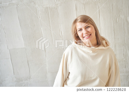 Smiling caucasian female adult in cream hoodie against textured wall background Smiling caucasian female adult in cream hoodie against textured wall background 122228628