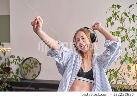 Young caucasian female dancing happily with headphones in cozy indoor setting Young caucasian female dancing happily with headphones in cozy indoor setting 122228686