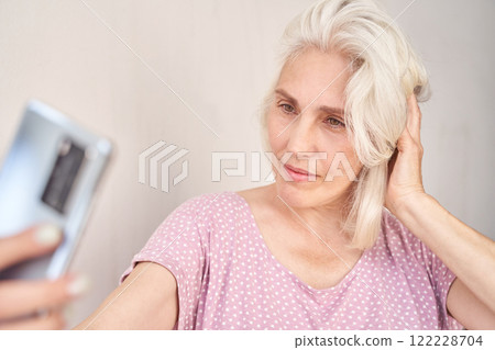 Elderly caucasian female taking selfie with smartphone in casual pink top 122228704