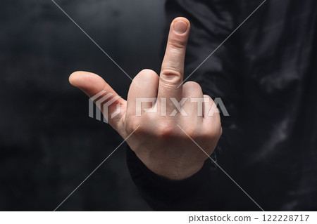 Man in a shirt showing a crude fuck gesture, middle finger sign, close-up against a concrete wall. Man in a shirt showing a crude fuck gesture, middle finger sign, close-up against a concrete wall. 122228717