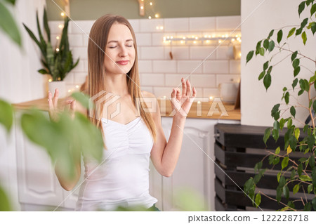 Young caucasian female practicing mindfulness meditation at home surrounded Young caucasian female practicing mindfulness meditation at home surrounded 122228718