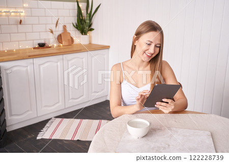 Young caucasian female adult using tablet in bright modern kitchen setting Young caucasian female adult using tablet in bright modern kitchen setting 122228739