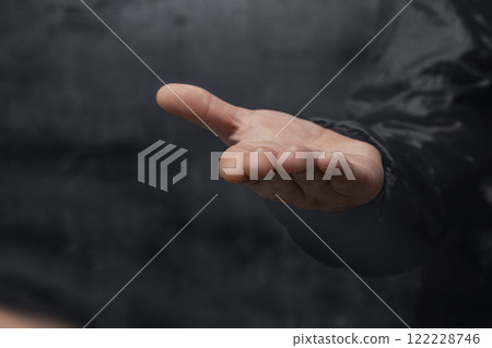 Close-up of a man in a sweater with his Open palm against on dark background. Close-up of a man in a sweater with his Open palm against on dark background. 122228746