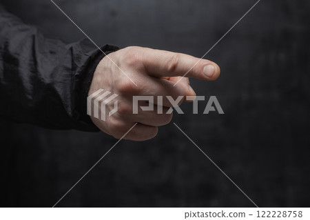 Concept of pointing finger. Close-up of a man in a sweater pointing his finger forward against on dark background. Concept of pointing finger. Close-up of a man in a sweater pointing his finger forward against on dark background. 122228758