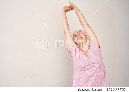 Elderly caucasian woman smiling and stretching in pink polka dot shirt against 122228762