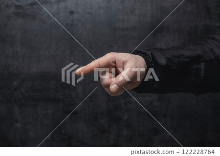 Concept of pointing finger. Close-up of a man in a sweater pointing his finger forward against on dark background. 122228764