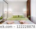 A well-appointed small modern bedroom with a cozy design, featuring a queen-sized bed, bedside tables. A large window with curtains allowing soft daylight. 122228878