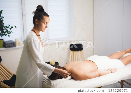 Massage therapist using Palo Santo stick at work with client who lying face down in salon, close-up, selective focus. Massage therapist using Palo Santo stick at work with client who lying face down in salon, close-up, selective focus. 122229971