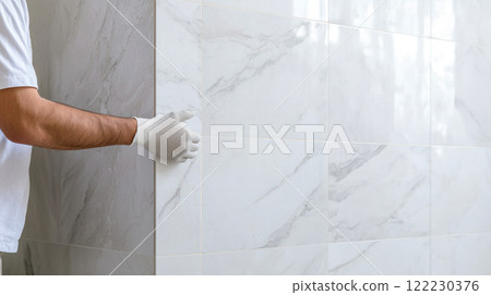 A master tiler checks the quality of laying ceramic tiles on a wall, finishing work on bathroom renovation 122230376