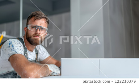 Professional tiler in safety glasses laying tiles, copy space for advertising construction work 122230379