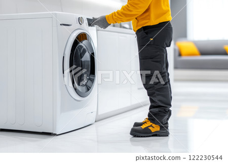 A man in work clothes professionally inspects household appliances installed at a client's house, copy space about services for service and maintenance of equipment A man in work clothes professionally inspects household appliances installed at a client's house, copy space about services for service and maintenance of equipment 122230544