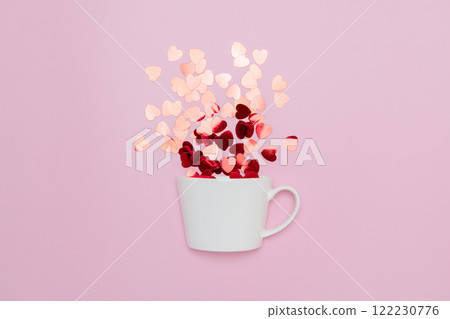 Creative minimalist composition of a white coffee cup spilling heart-shaped confetti, set against a pink background, symbolizing love and warmth. 122230776
