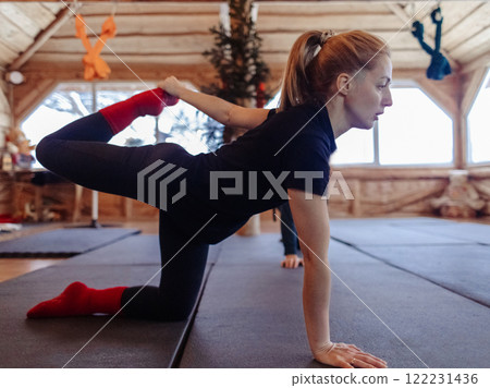 A yoga teacher shows students how to do an asana correctly. A young woman teaches yoga and helps with poses during a class in a spacious studio 122231436