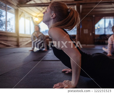A yoga teacher shows students how to do an asana correctly. A young woman teaches yoga and helps with poses during a class in a spacious studio 122231523