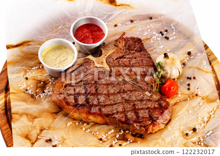 T bone fresh juicy steak served with ketchup and sauce at a wooden board isolated at white background. 122232017