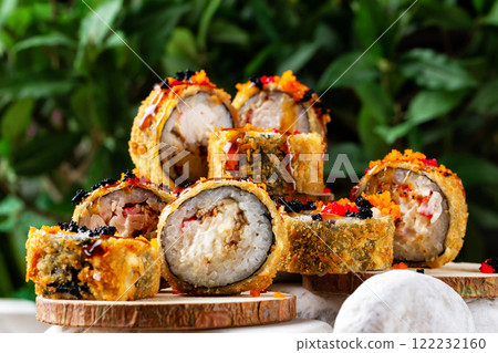 Closeup set of hot tempura sushi rolls with eel, cheese, crab and caviar at small wooden boards on stones at decorated green background. 122232160