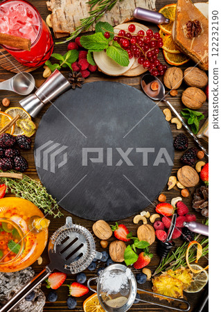 Top view image image of tea ceremony with natural food ingredients around - berries,. nuts and kitchenware at wooden table background with a round stone board at centre. Top view image image of tea ceremony with natural food ingredients around - berries,. nuts and kitchenware at wooden table background with a round stone board at centre. 122232190