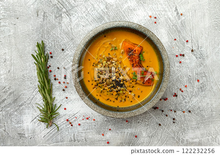 Plate of healthy pumpkin soup deorated with chia seeds and nuts at concrete background with spices and rosemary. Plate of healthy pumpkin soup deorated with chia seeds and nuts at concrete background with spices and rosemary. 122232256
