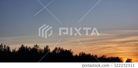 Sunset, blue skies, flying plane behind leaving traces. 122232311