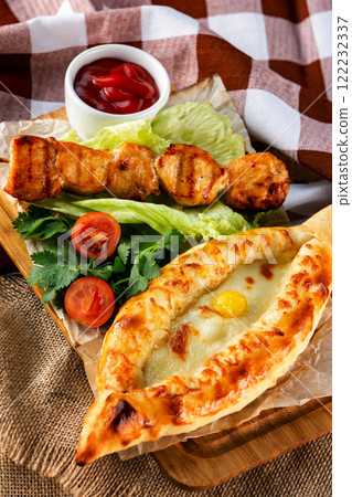 Traditional georgian adzharian khachapuri and meat shashlik with vegetables at decorated wooden board background. Traditional georgian adzharian khachapuri and meat shashlik with vegetables at decorated wooden board background. 122232337