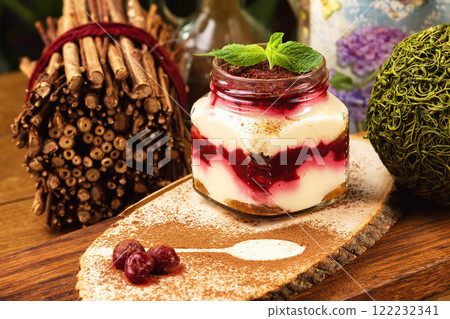 Closeup glass jar of cream cheese parfait with whipped cream and strawberry jam sereved with mint and chocolate at decorated wooden board background. Closeup glass jar of cream cheese parfait with whipped cream and strawberry jam sereved with mint and chocolate at decorated wooden board background. 122232341