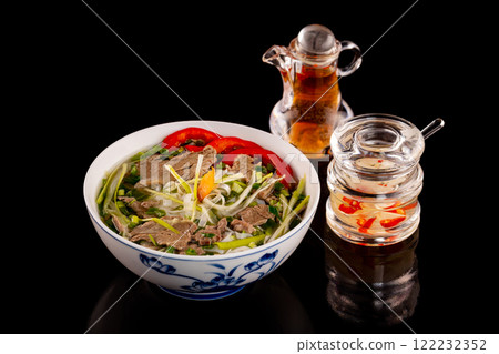 Bowl of vietnamese traditional soup pho with beef meat served with sauces isolated at black background. Bowl of vietnamese traditional soup pho with beef meat served with sauces isolated at black background. 122232352