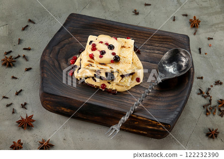 Closeup image of millefeulle with prunes and wild berries served with a spoon at wooden tray at concrete background. Closeup image of millefeulle with prunes and wild berries served with a spoon at wooden tray at concrete background. 122232390