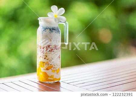 Pitcher of superfood layered smoothie with tropical fruits and berries at wooden table at green tropical blurred background with copyspace. Pitcher of superfood layered smoothie with tropical fruits and berries at wooden table at green tropical blurred background with copyspace. 122232391