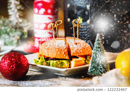 Closeup image of hamburger on white plate at Christmas style decorated wooden background with falling snow bokeh. 122232467