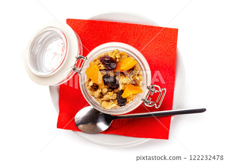 Top view image of an opened creamy granola jar with nuts and dried fruits on a plate with a napkin isolated at white background. Top view image of an opened creamy granola jar with nuts and dried fruits on a plate with a napkin isolated at white background. 122232478