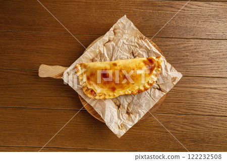 Yellow crispy khachapuri on a cooking paper on a wooden tray at brown table background. Yellow crispy khachapuri on a cooking paper on a wooden tray at brown table background. 122232508