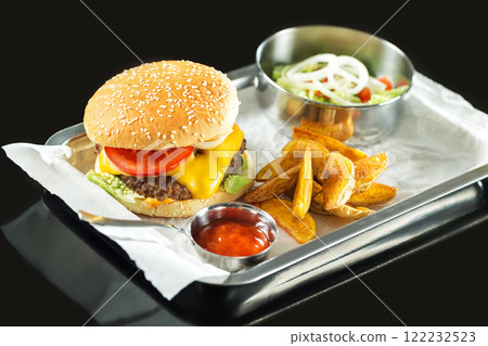 Closeup fast food set including hamburger, ketchup, salad and french fries on a tray at black background. 122232523