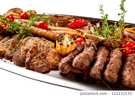Closeup metal dish with grilled meat assortment and vegetables isolated at white background. 122232533
