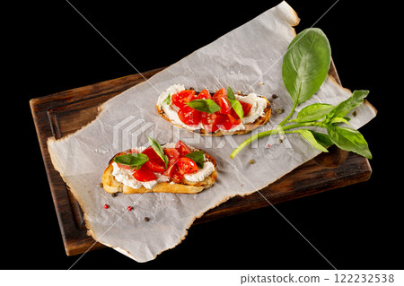 Italian bruschetta with cream cheese, tomatoes and basil at wooden board isolated at black background. Italian bruschetta with cream cheese, tomatoes and basil at wooden board isolated at black background. 122232538
