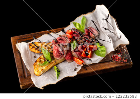 Roast beef served with homemade ciabatta, tomatoes and balsamic sauce on wooden board isolated at black background. 122232588