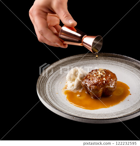 Closeup square image of plate with sweet muffin cake and icecream isolated at black background with copyspace. Male hand with jigger pouring caramel and decorating the pastry. 122232595