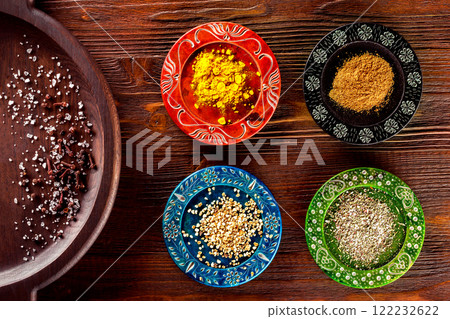 Closeup image of colorful ethnic style plates with spices at wooden table background. 122232622