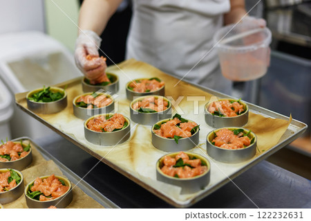 Female cook is filling group of tarts with salmon at restaurant kitchen background. Culinary process Female cook is filling group of tarts with salmon at restaurant kitchen background. Culinary process 122232631