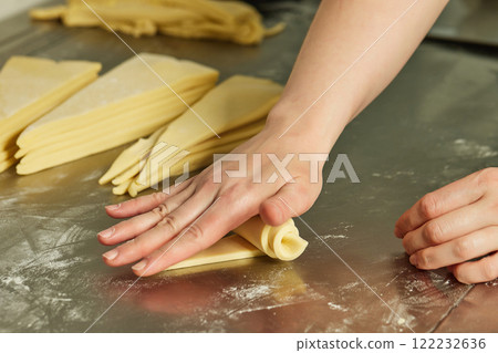 Female hand is rolling croissant dough at restaraunt kitchen. Closeup image of bakery process 122232636